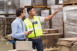 Warehouse worker showing something to his manager in a large warehouse